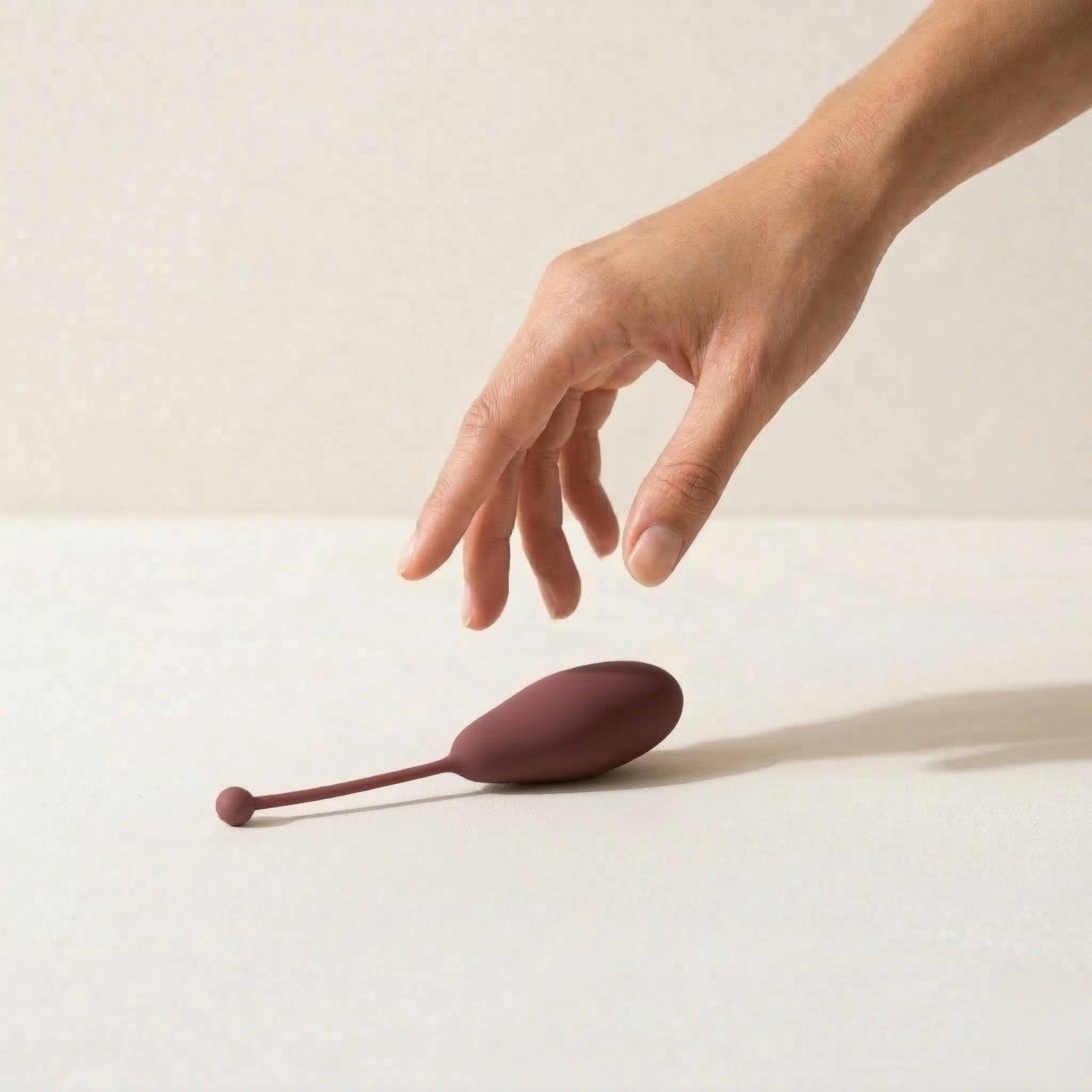 Hand reaching toward a dark weight on a clean surface — precision and intention
